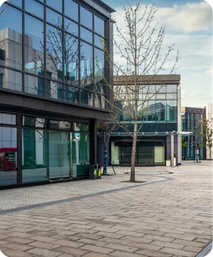 Modern office buildings around a paved plaza with young trees.