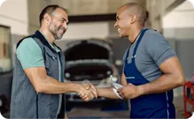 A mechanic shakes hands with a customer in a garage.