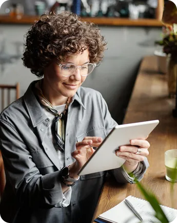 A woman in a cafe smiling at a tablet.