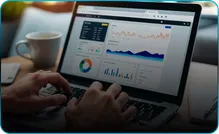 Hands type on a laptop showing charts, beside a cup of coffee.