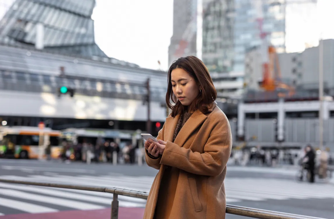 A woman on a city street looks at her phone.