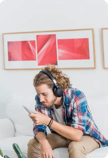 A man in headphones listens on his phone at home.