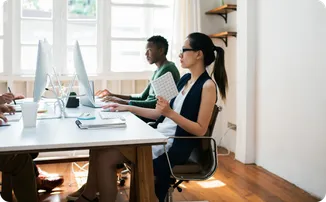 Two people work at computers in a bright office.
