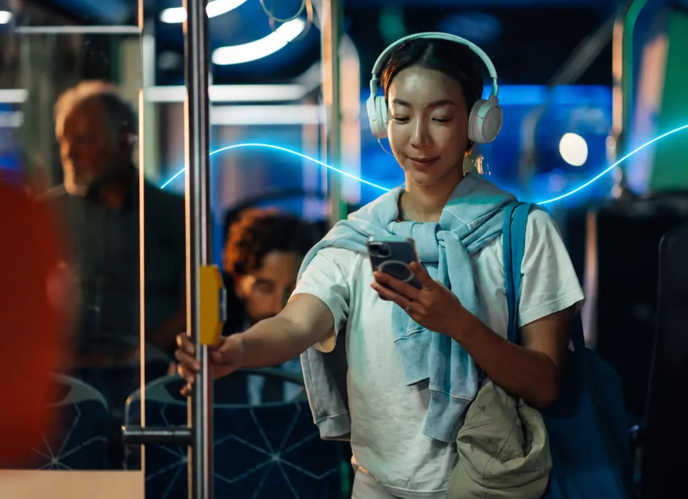 A woman with headphones looking at her phone on a bus at night.