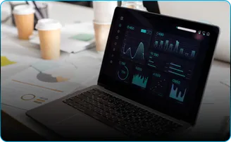 A laptop shows a dashboard of charts beside paper coffee cups.