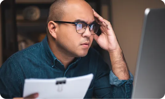 A man frowning at a laptop, his hand on his head.