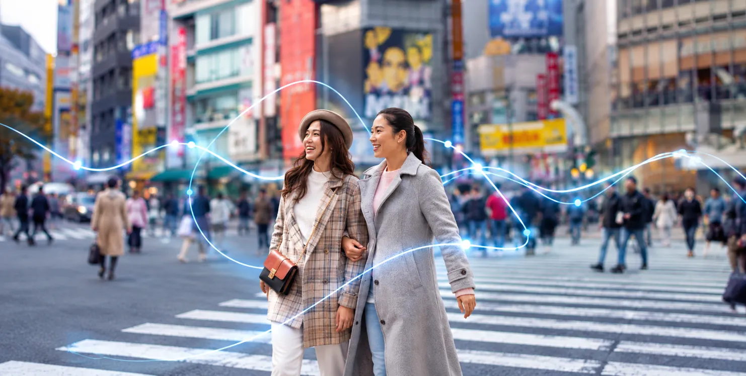Two women walking arm in arm along a busy city street.