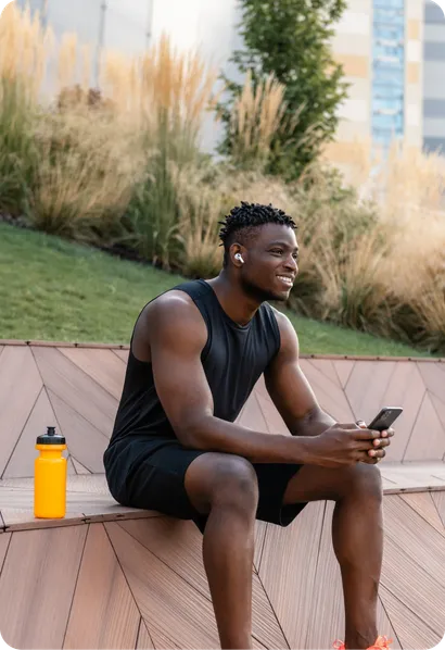 A man in sportswear sits outdoors with his phone after training.