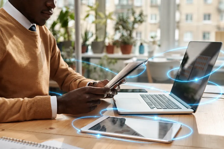 Hands on a laptop and a phone at a desk, with blue light trails around them.
