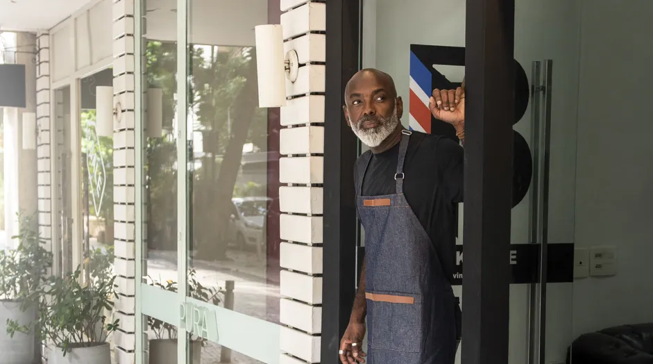 A man in an apron stands in a shop doorway.