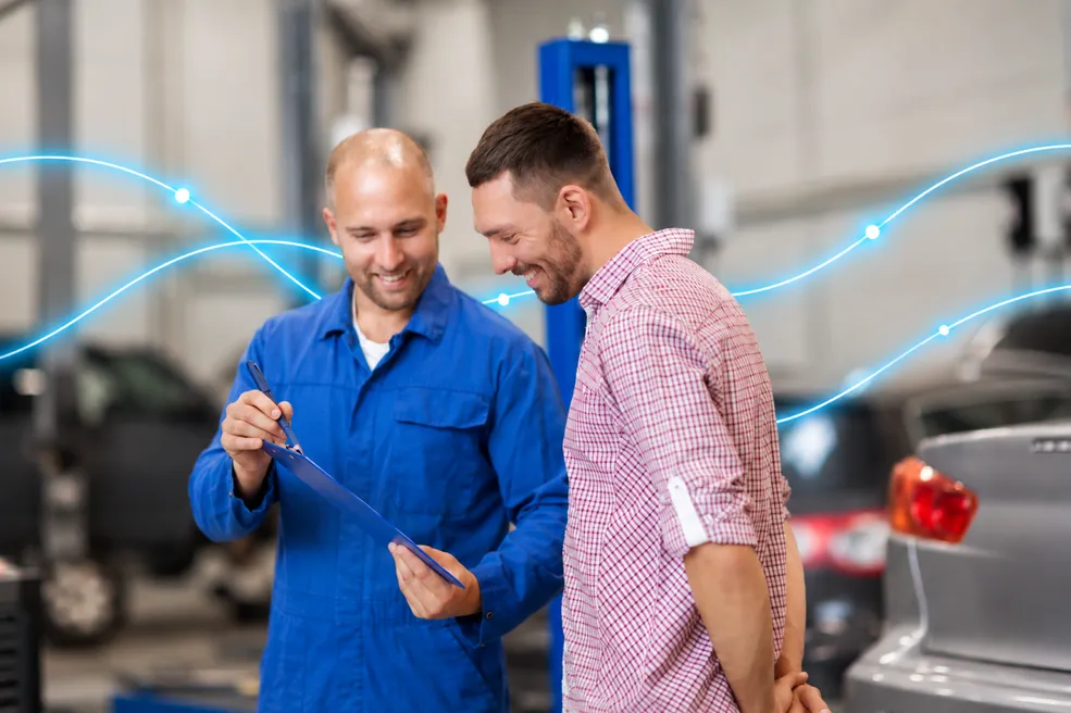 Two men in a repair garage smiling over a clipboard.