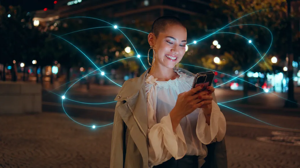 A woman smiling at her phone on a city street at night.