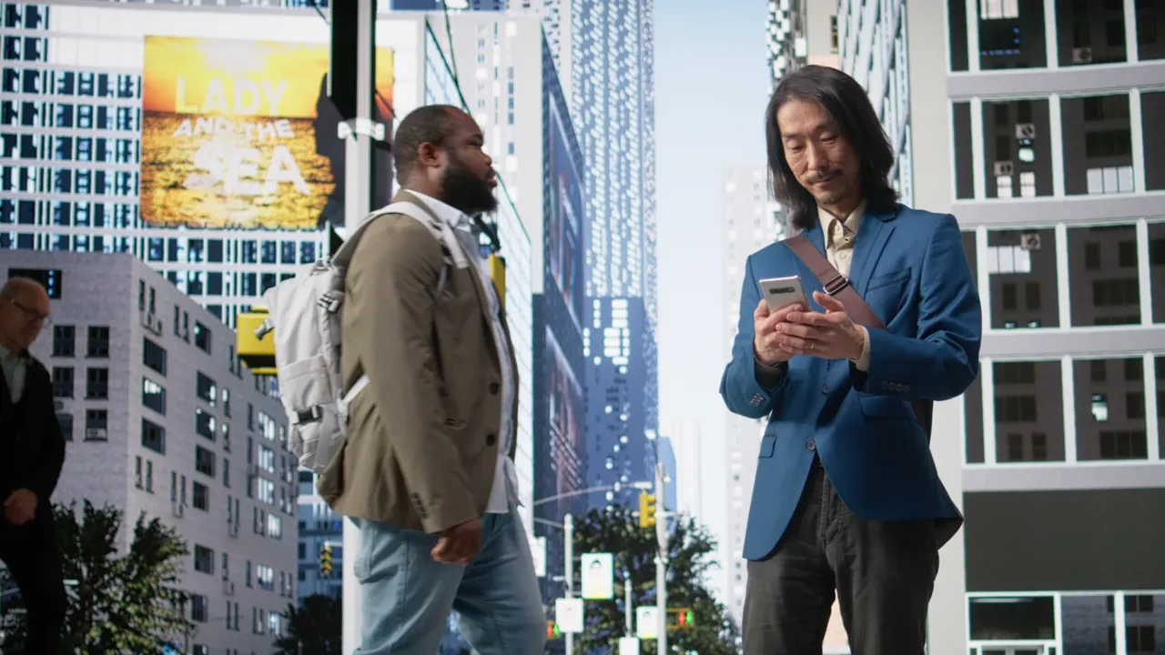 A man in a blue jacket reads his phone on a city street.