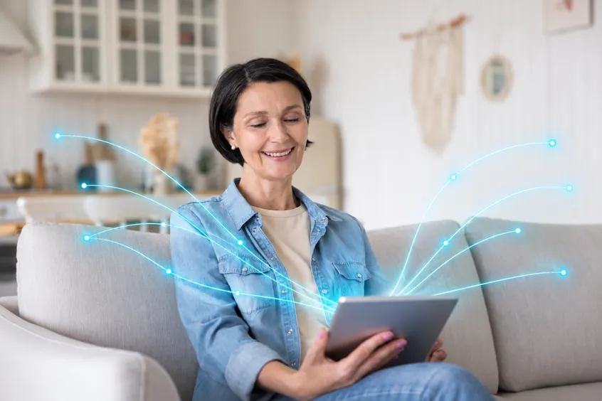 A smiling woman holds a tablet at home, with lines of light around her.