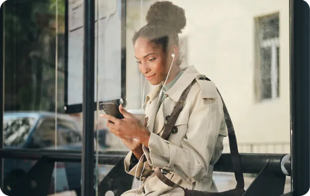 A woman in a trench coat smiling at her phone.