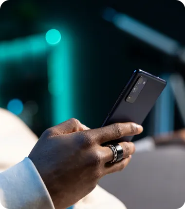 A hand holds a phone in front of a city street at night.