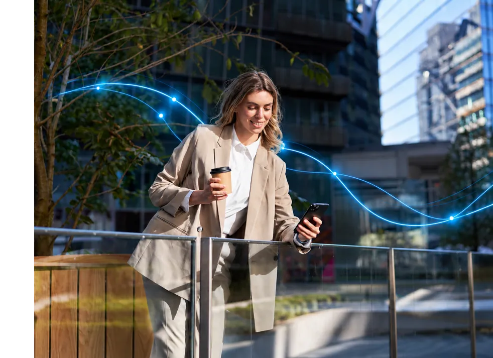 A woman with a coffee checking her phone on a city street at sunset.