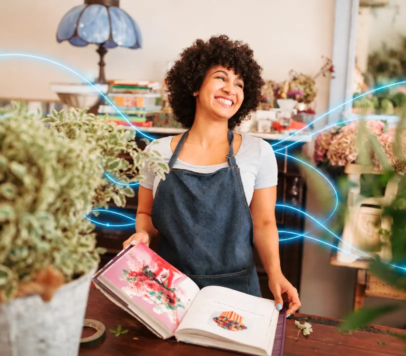 A smiling woman in an apron holding open a catalogue in a shop.