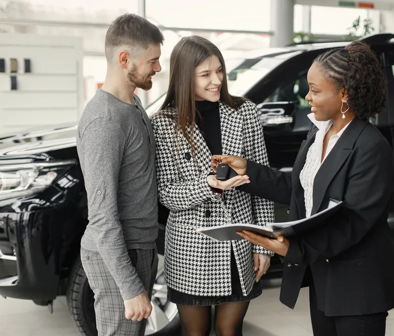 A car salesperson hands a young couple the keys.