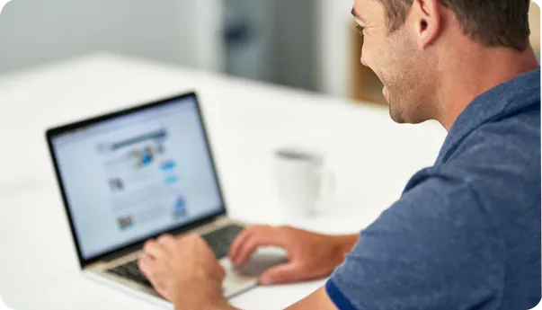 A man smiling at a laptop showing a search page.