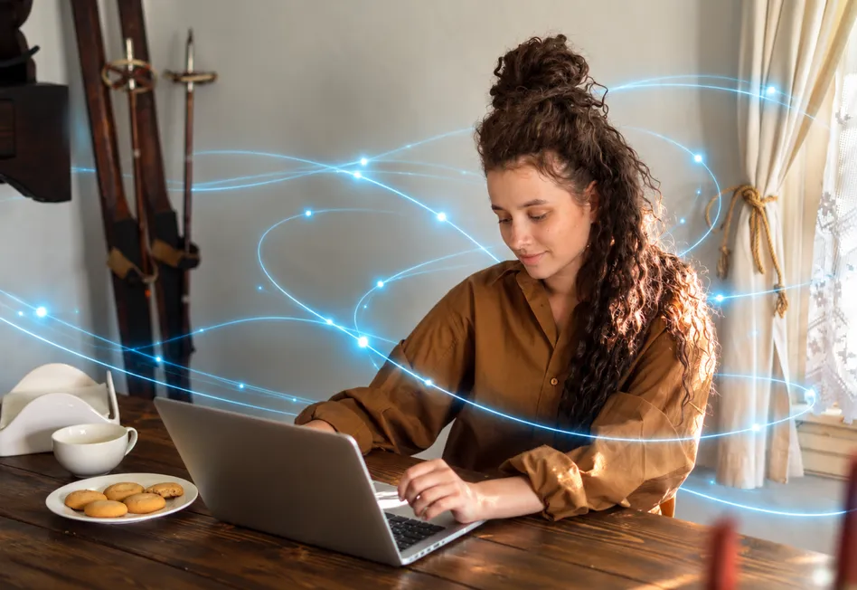 A woman with curly hair smiles at her laptop, with lines of light circling her.