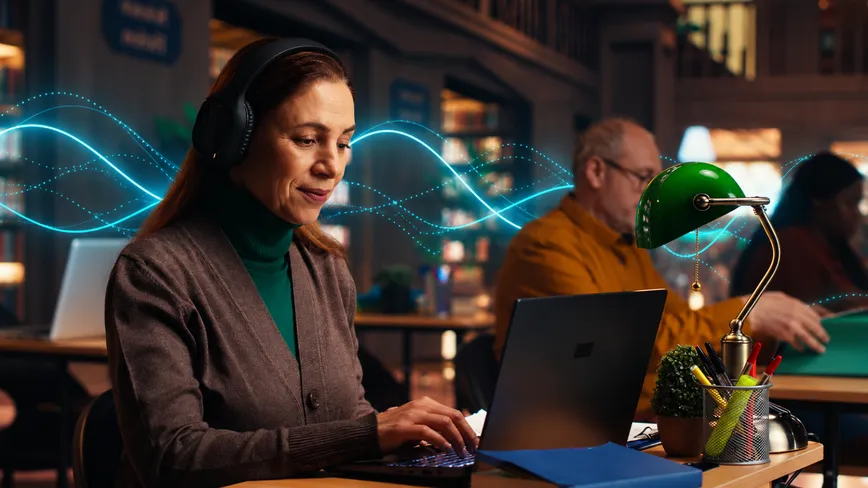 A woman in headphones works on a laptop in a library, with sound waves drawn around her.