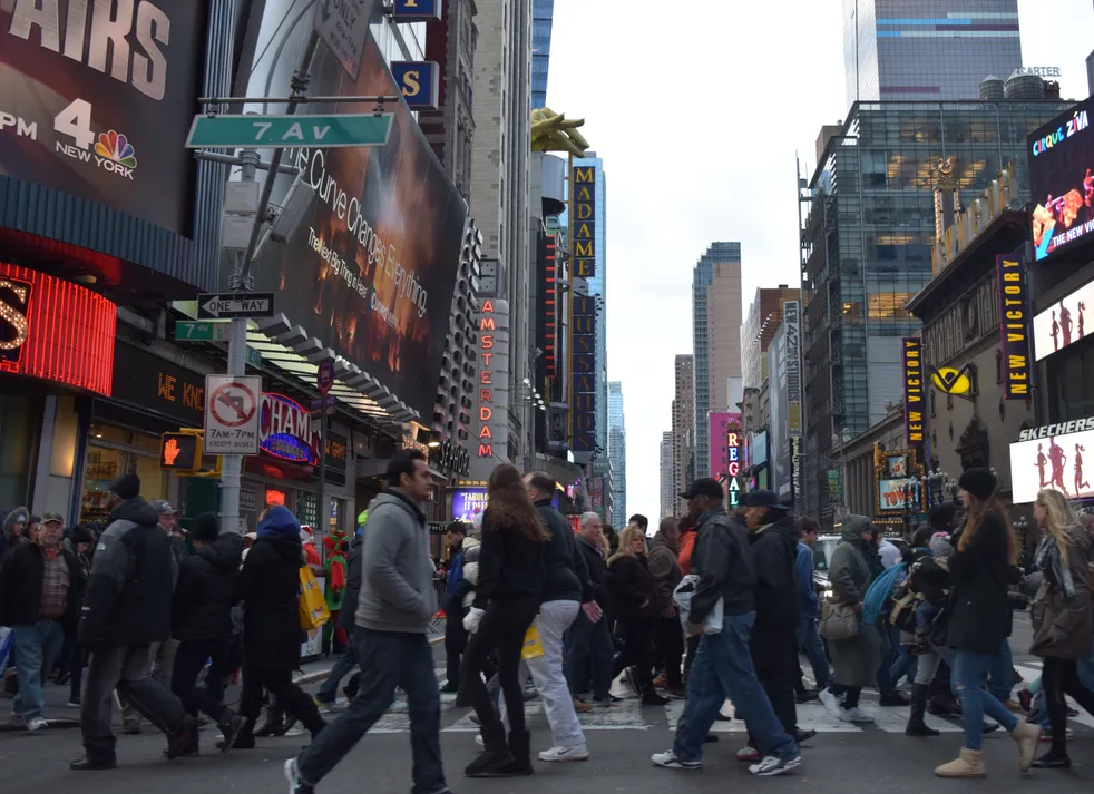 Crowds crossing a busy city street lined with shop signs.