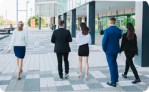 People in business clothes walk across a plaza between office buildings.