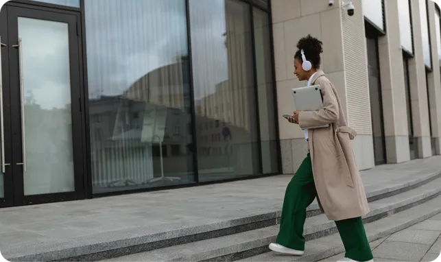 A woman with headphones walking up steps outside an office building.