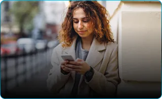 A woman in a cream coat reads her phone on a city street.