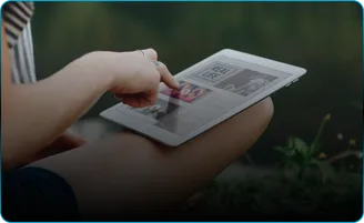 A woman outdoors reading on a tablet.
