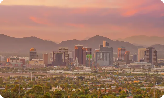 The Phoenix skyline under a pink evening sky, with mountains behind.