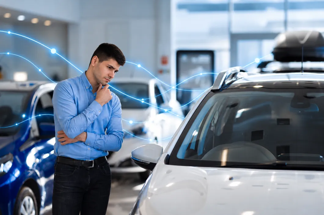 A man in a car showroom, thinking as he looks at a car.