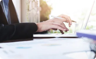 A hand writes with a pen beside a laptop.