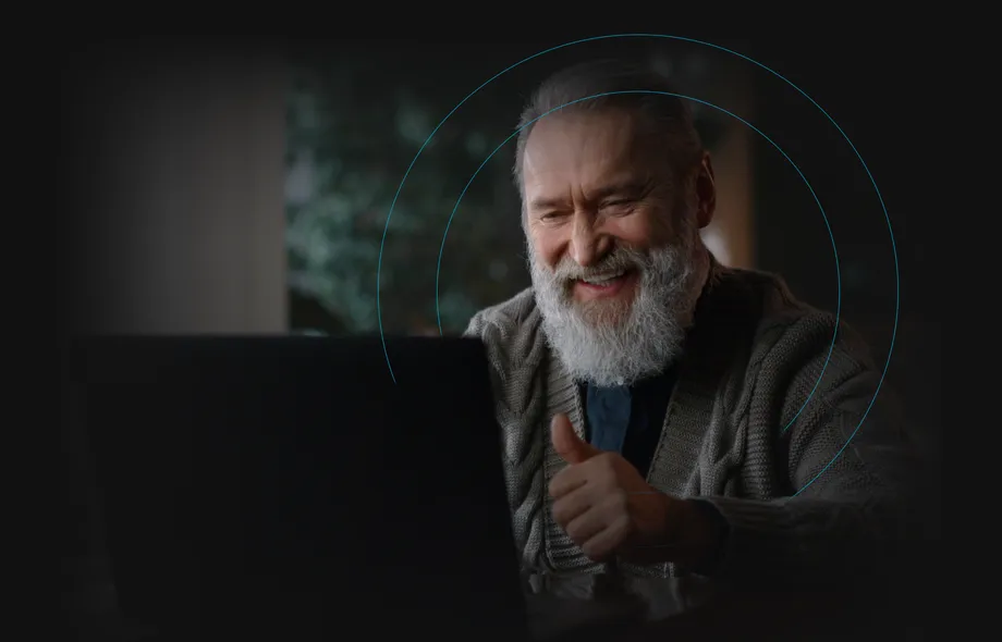 A smiling older man giving a thumbs up at his laptop.
