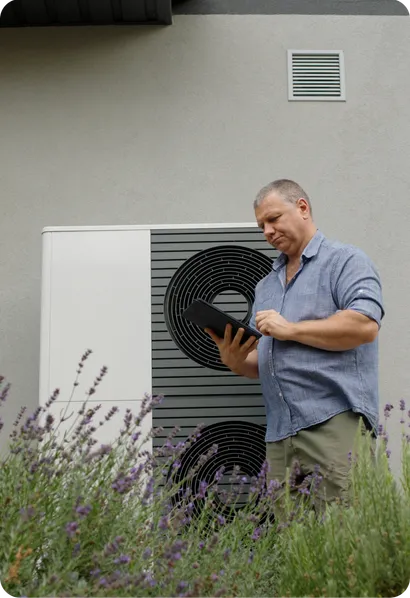 A man checks a heat pump with a tablet among lavender plants.