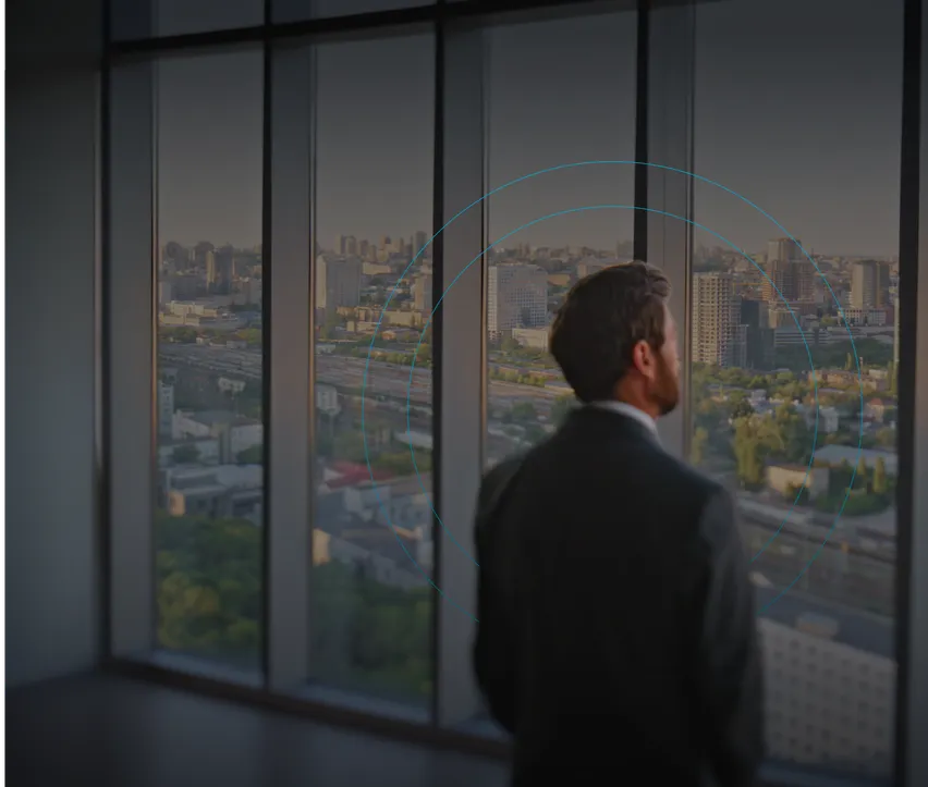 A man in a suit looks out over a city from an office window.